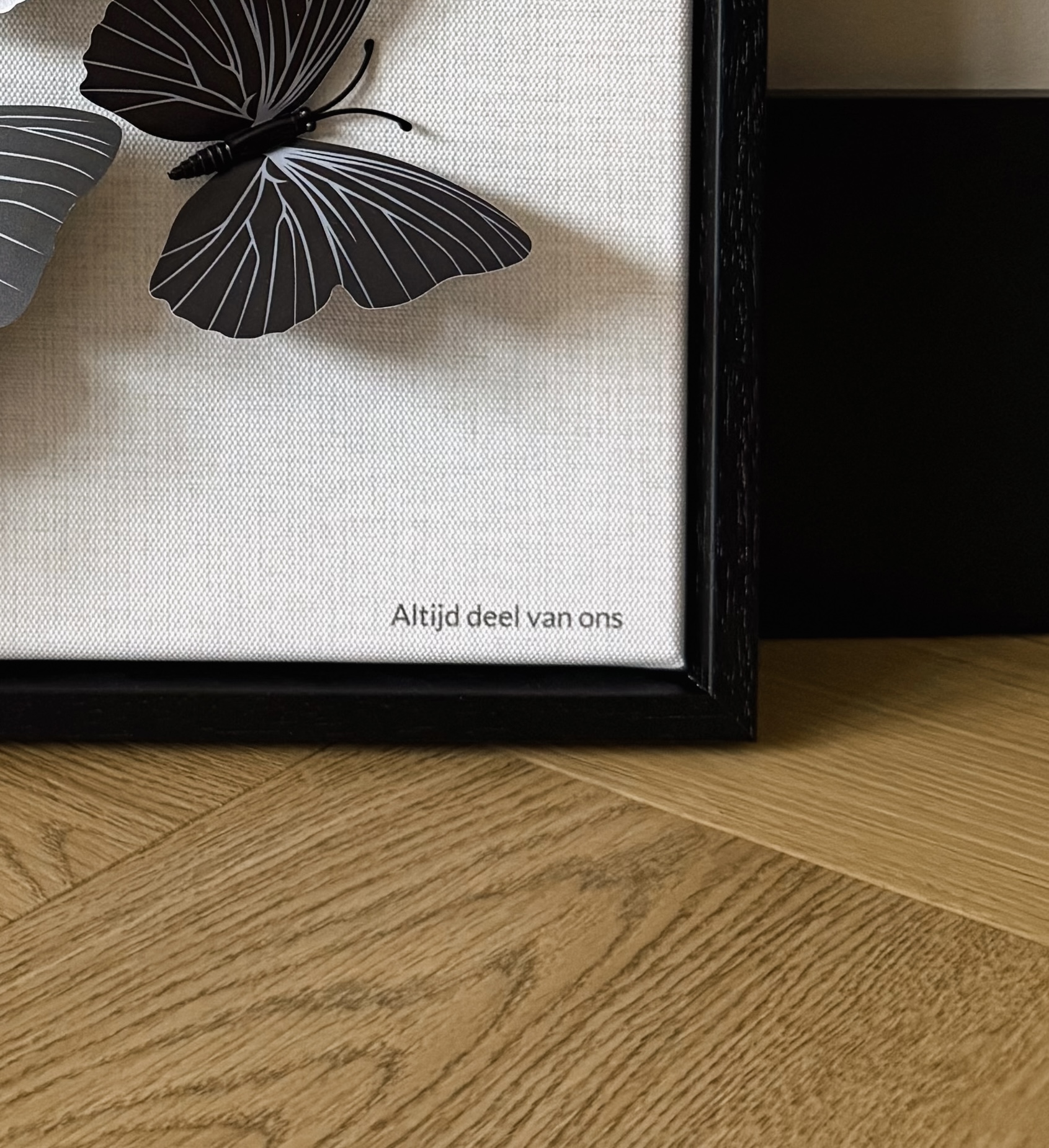 Detail van een wanddecoratie met zwarte vlinders en de tekst Altijd deel van ons
